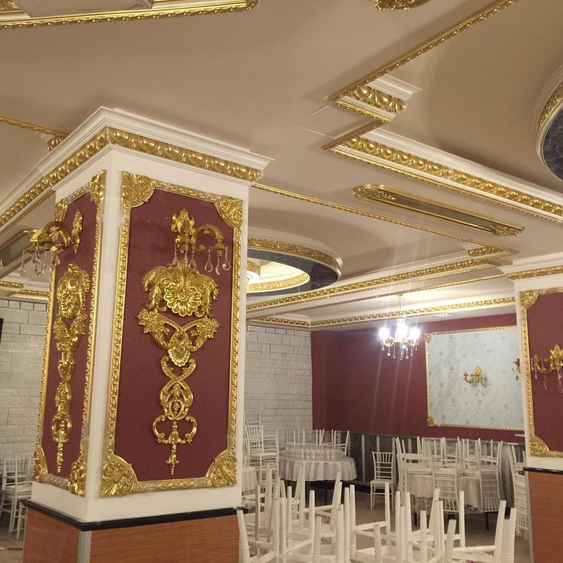 Interior de sală de evenimente cu cornișe aurite, aplice pe stâlp bordo și candelabre de cristal