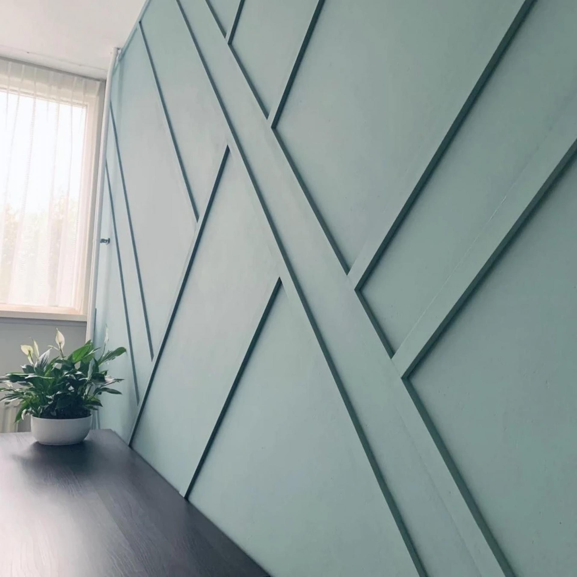 Perete de accent verde-mentă cu lamele geometrice diagonale din poliuretan lângă o fereastră