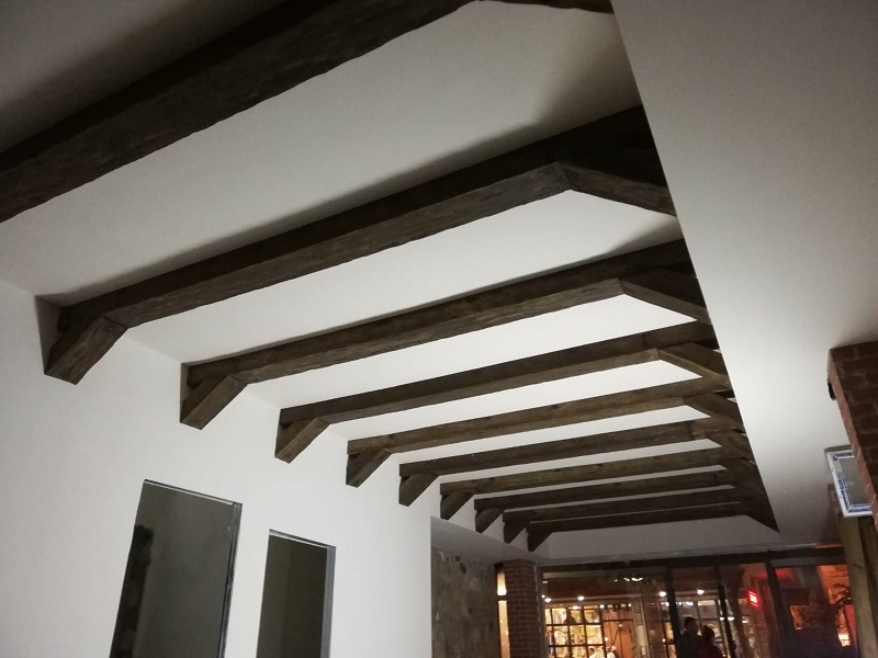 Tavan alb cu grinzi decorative de lemn aparente într-un spațiu comercial cu vitrină