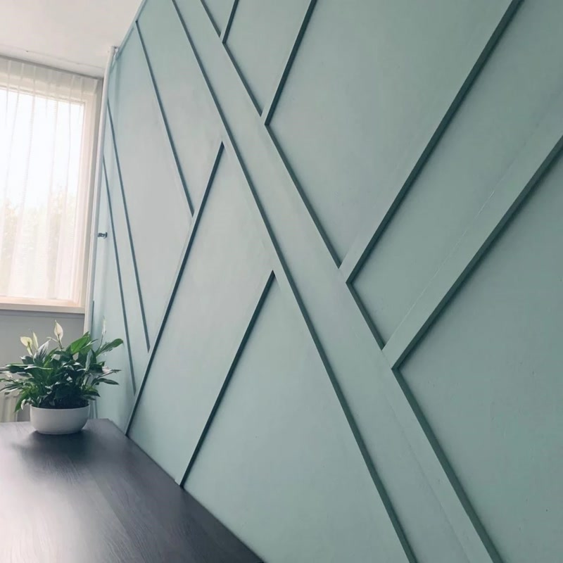 Perete de accent verde-mentă cu lamele geometrice diagonale din poliuretan lângă o fereastră