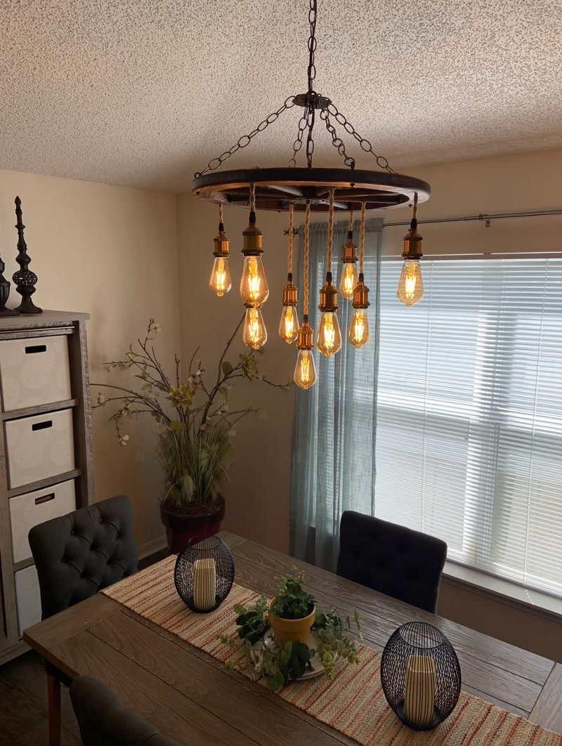 Candelabru rustic în formă de roată cu becuri Edison deasupra unei mese