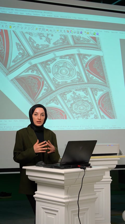 Designerul explică soluția flexibilă lângă proiecția tavanului ornamental.