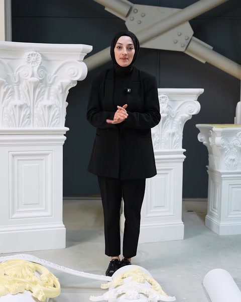 Femeie stă în picioare printre coloanele decorative albe din showroom.