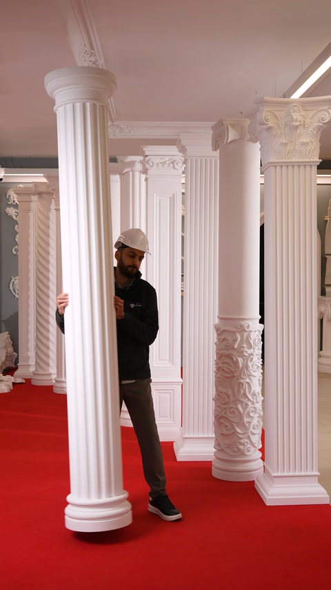 Bărbatul prezintă o coloană canelată cu capitel într-un showroom decorativ.