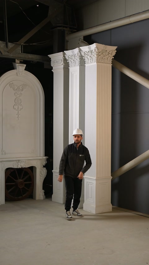 Prezentatorul se află lângă trei pilastri cu modele distincte.