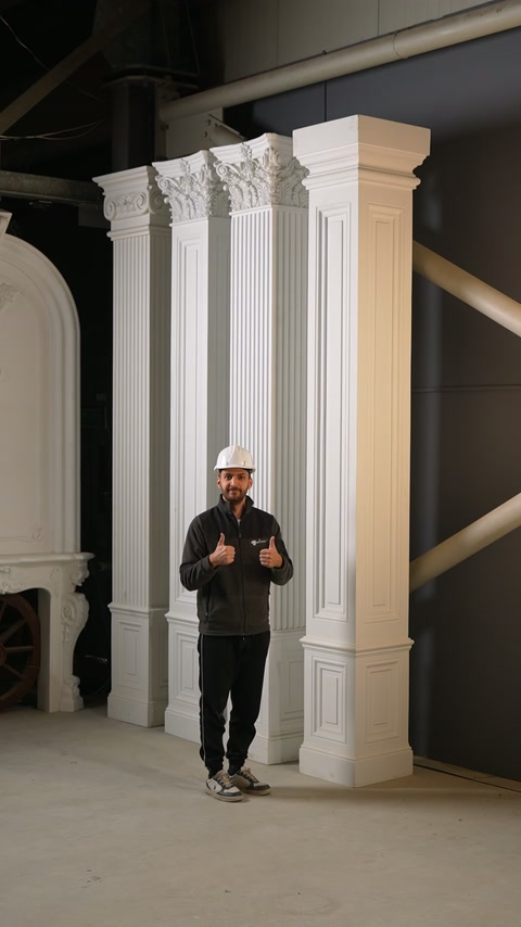 Prezentatorul gesticulează în fața unui șir de pilastri monumentali.