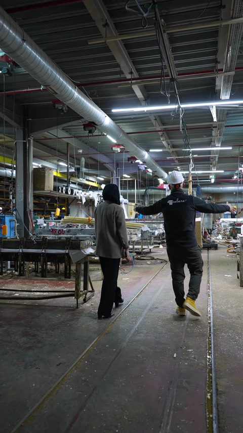 Angajată traversează hala de producție printre utilaje și rafturi